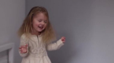 Güzel küçük kız eğleniyor, gri yatak odasında yatağa atlıyor. Sabah rutini, çocukluk, kız. Tam HD görüntüler