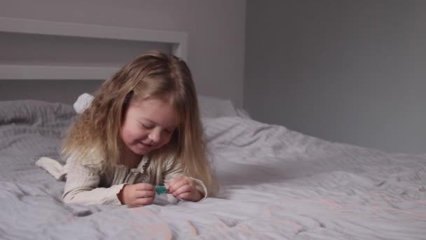 Mooi klein meisje vangen kleine kerstbomen liggend op bed in grijze slaapkamer. Nieuwjaar, jeugd, dochter. FullHD-beelden — Stockvideo