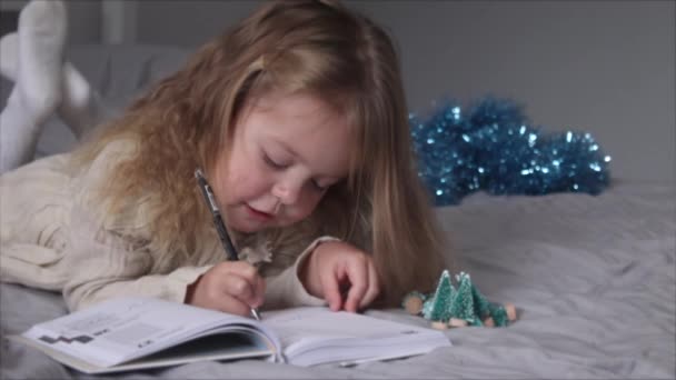 Urocza dziewczynka pisząca list do Świętego Mikołaja na łóżku w szarej sypialni. Nowy rok, dzieciństwo, Boże Narodzenie. Nagrania w Full HD — Wideo stockowe