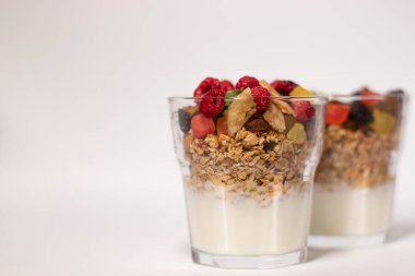 Yoğurt ve şekerli müsli tatlı ya da beyaz arka planda izole edilmiş bardakta ahududu ile kurutulmuş meyve. Granola kahvaltısı