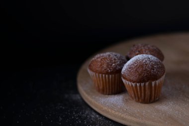 Tahta tezgahta toz şekerle kaplı üç muffin siyah arka planda izole edilmiş. pastane tatlı