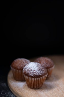 Tahta tezgahta toz şekerle kaplı üç muffin siyah arka planda izole edilmiş. pastane tatlı