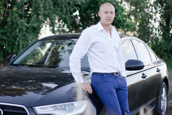 handsome bald man in a suit near luxury car. businessman in automobile