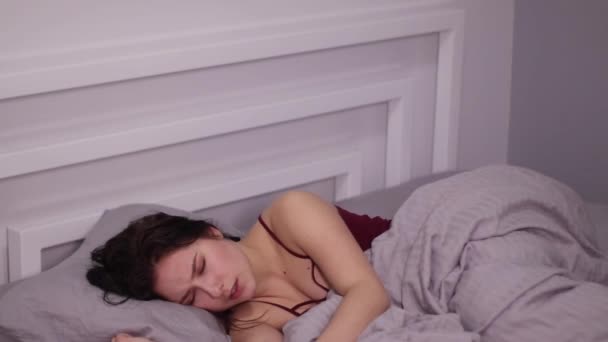 灰色のシーツのベッドで官能的な美しいブルネットの女性は 夢と思考を持って寝て — ストック動画