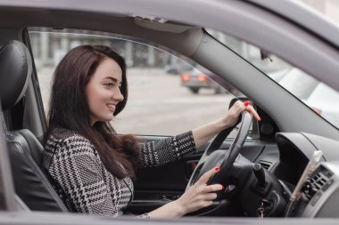 Siyah bir arabada gri kareli elbiseli çekici bir esmerin portresi. Otomobildeki kız. iş kadını