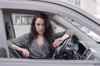 Siyah bir arabada gri kareli elbiseli çekici bir esmerin portresi. Otomobildeki kız. iş kadını