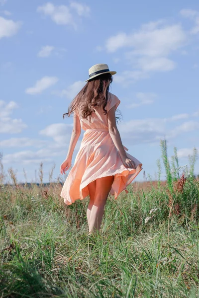 pretty brunette woman in cream dress and a straw hat in the field