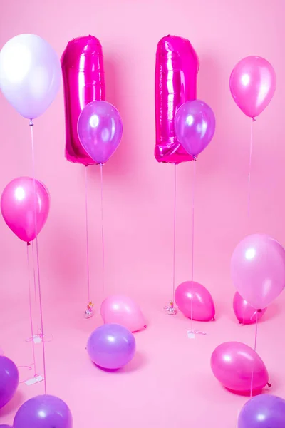 colorful blue, pink and purple balloons near air balloons shaped number eleven . on pink background. concept of birthday party celebration.