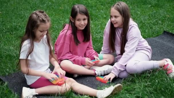 3 Mädchen spielen mit trendigem Sinnesspielzeug, das es draußen auf dem Gras knallen lässt. Push Pop Blase flexibles Fidget sensorisches Spielzeug. Stress- und Angstabbau. Silikonspiel für gestresste Kinder und Erwachsene. extra Zeitlupe — Stockvideo