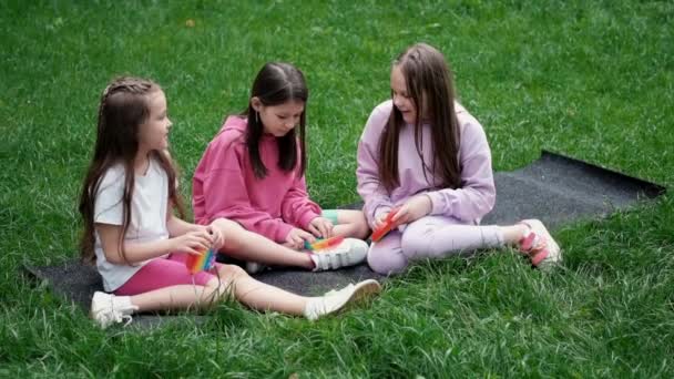 3 girls play with trendy sensory toy pop it outdoors on grass. Push pop bubble flexible fidget sensory toy. Stress and anxiety relief. silicon game for stressed children and adults. extra slow motion — Stock Video