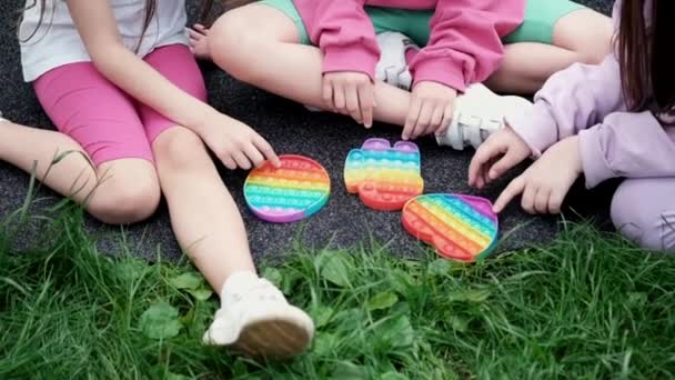 3 chicas adolescentes en ropa colorida juegan con el juguete sensorial de moda pop it outdor. burbujas de silicona suave arco iris. alivio de la ansiedad, antiestrés, concepto de salud mental. Anti estrés popit juego. cámara lenta — Vídeo de stock