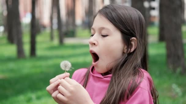Retrato de uma linda adolescente soprando no dente-de-leão amadurecido em um parque de primavera ou verão. câmera lenta de vídeo — Vídeo de Stock