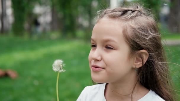 Портрет красивої дівчини-підлітка, що дме на стиглій кульбабі в весняному або літньому парку. повільне відео руху — стокове відео