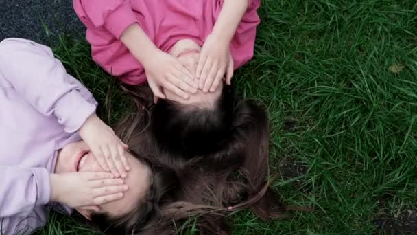 Two pretty millennial kids friends lying on green grass in park or lawn. Caucasian girls smiling and having fun together. Footage from the top view — Stock Video