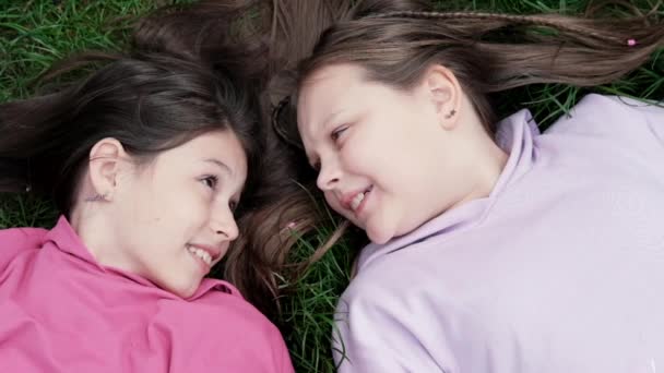 Dwoje milenijnych przyjaciół leżących na zielonej trawie w parku lub na trawniku. Białe dziewczyny uśmiechające się i bawiące razem. Nagranie z widoku z góry — Wideo stockowe