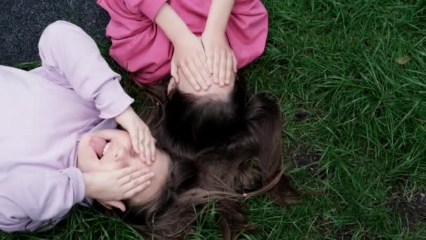 Deux jolies amies millénaires allongées sur de l'herbe verte dans un parc ou une pelouse. Filles caucasiennes souriant et s'amusant ensemble. Images de la vue du haut — Video