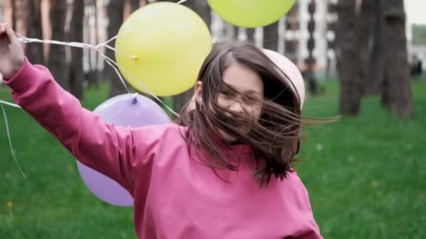 Sladká brunetka dospívající dívka v růžové mikině baví s horkovzdušnými balónky. Veselé letní dny, prázdniny, prázdniny. zpomalený pohyb — Stock video