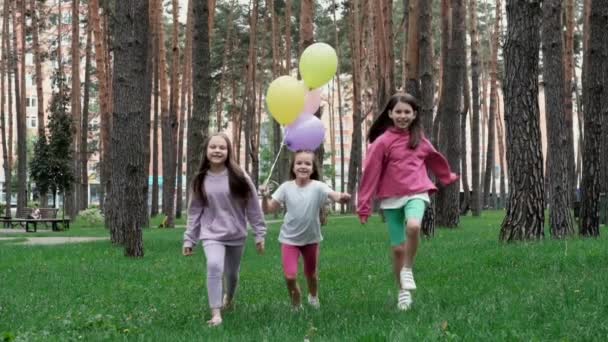 krásné děti dívky venku s barevnými balónky. Šťastné děti pobíhající na zelené trávě s balónky v rukou. koncepce svobody, dětského snu, šťastné rodiny. Sestry, nejlepší kamarádky. zpomalený pohyb.