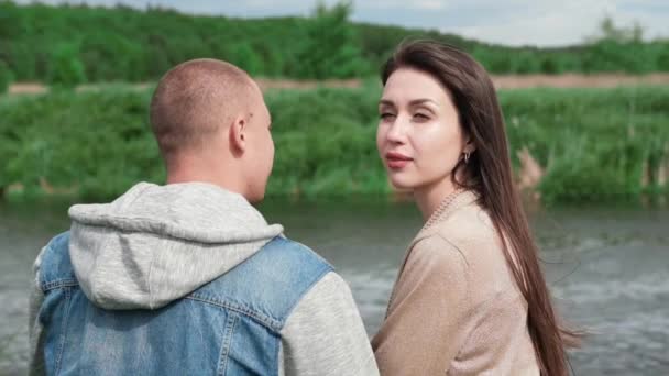 Dolce coppia seduta vicino al fiume d'acqua su erba verde. attraente donna bruna e uomo calvo all'aperto. vero amore, famiglia felice, romanticismo, matrimonio di successo. rallentatore — Video Stock