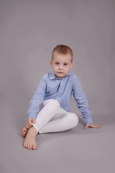 Předškolní Blondýny Chlapec Bílých Kalhotách Modré Košili Šedém Pozadí Dítě — Stock fotografie