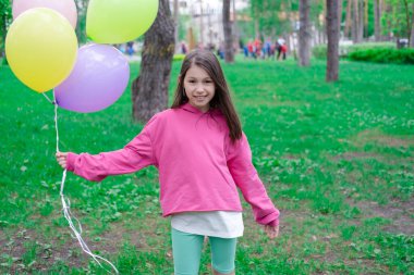 Açık havada elinde renkli balonlar tutan pembe elbiseli tatlı esmer kız. Parti, doğum günü konsepti. Yaz zamanı. Mutlu çocuklar..