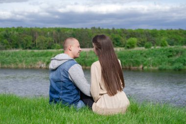 Su nehrinin kenarında yeşil çimlerin üzerinde oturan tatlı bir çift. Çekici esmer kadın ve kel adam dışarıda. Gerçek aşk, mutlu aile, romantizm, başarılı evlilik.