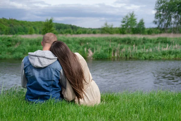 Su nehrinin kenarında yeşil çimlerin üzerinde oturan tatlı bir çift. Çekici esmer kadın ve kel adam dışarıda. Gerçek aşk, mutlu aile, romantizm, başarılı evlilik.