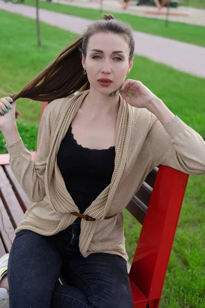 Retrato de mujer morena con ponyrail sentado en un banco en el parque. amantes de la naturaleza, chica atractiva. — Foto de Stock