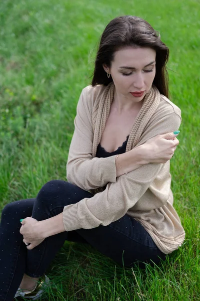 Krásná brunetka žena sedí na zelené trávě — Stock fotografie