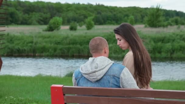 Hermosa pareja joven sentada en un banco en el parque. conversación, comunicación, relación. matrimonio feliz, amor verdadero. cámara lenta — Vídeo de stock