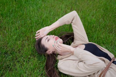 Çekici esmer yeşil çimlerin üzerinde yatıyor. Yorgun, ciddi..