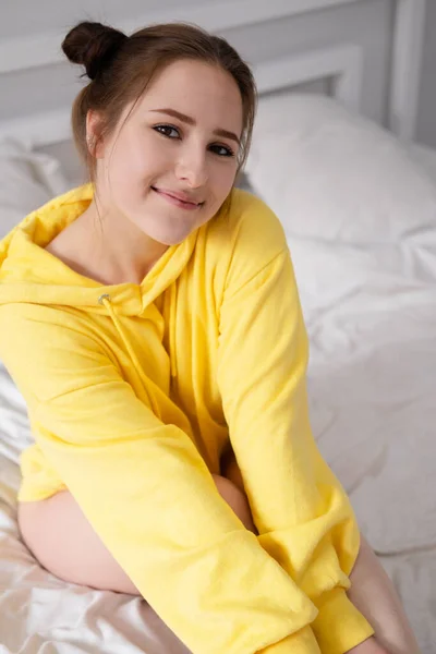 快乐快乐的黑发姑娘 穿着黄色的连帽衫 躺在白床床上 — 图库照片