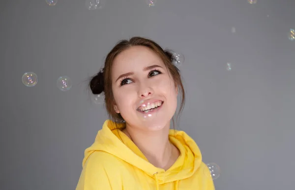 Gelukkig Brunette Vrouw Geel Hoodie Tussen Zeepbellen Heldere Grijze Kamer — Stockfoto