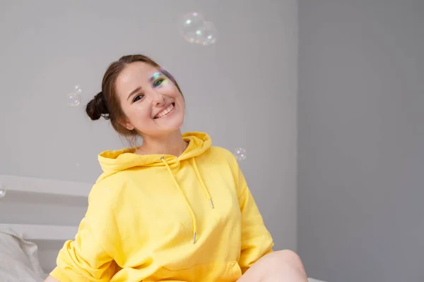 Gelukkig Brunette Vrouw Geel Hoodie Tussen Zeepbellen Heldere Grijze Kamer — Stockfoto