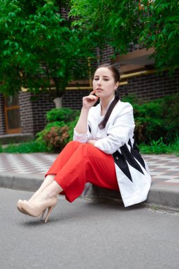 Açık havada poz veren kırmızı ve beyaz elbiseli çekici esmer kadın. Yaz mevsimi, yeşil ağaçlar.