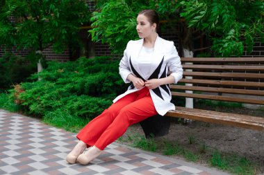 Açık havada poz veren kırmızı ve beyaz elbiseli çekici esmer kadın. Yaz mevsimi, yeşil ağaçlar.