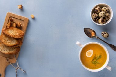 Mavi zemin üzerinde kızarmış ekmek, kızarmış ekmek, kızarmış ekmek, ekmek, kaşık, maşa ve yumurtalarla birlikte beyaz fonda bulyon, bıldırcın yumurtası ve rezene yaprağı ile yatıyordu. Ev yapımı sağlıklı beslenme ve beslenme. Boşluğu kopyala.