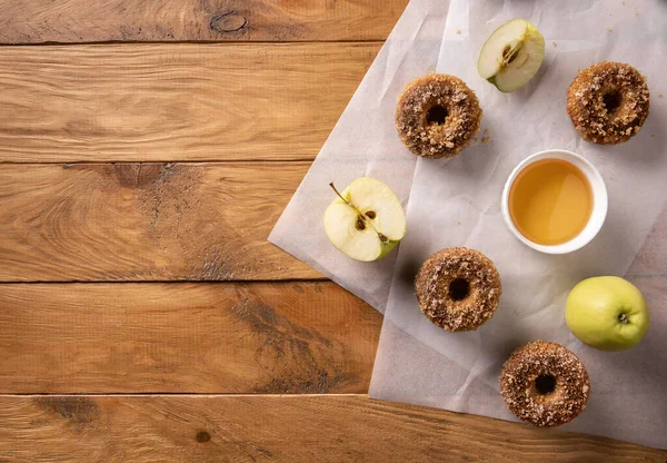 Baked apple cider donuts with apple cider and fruits on baking sheets on natural wooden table. Ready to eat snack. Small batch of homemade food. Directly above view. Horizontal orientation. Copy space