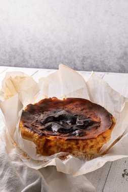 Lezzetli bask peynirli keki keten peçete ve desenli beyaz ahşap masa üzerinde pişirme kağıdında yaktı. Seçici odaklanma. İspanya 'nın San Sebastian şehrinden ev yapımı İspanyol tatlısı. Büyük kopyalama alanı.