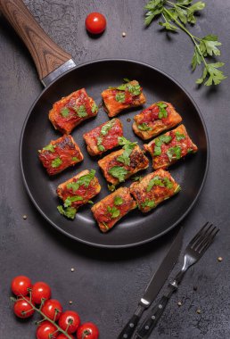 Domates soslu ev yapımı lahana ruloları ve tavada taze doğranmış maydanoz. Lahana ruloları, domatesler, maydanozlar, metal çatal ve bıçakla kaplı düz bir zemin..