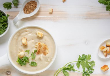 Beyaz karnabahar kremalı çorba, şifalı otlar ve ahşap masada beyaz kase içinde kızarmış ekmek. Tabak ve malzemeleri beyaz çanak çömlek içinde yemeye hazır bir şekilde yatıyordu. Uzayı kopyala Yatay yönelim.