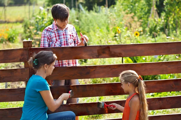 Frau und Kinder streichen den Gartenzaun — Stockfoto