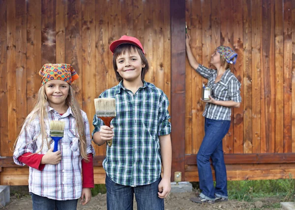 Kinder helfen ihrer Mutter beim Streichen des Holzschuppens — Stockfoto