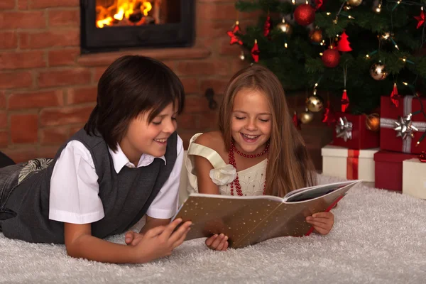 Crianças lendo um livro - na frente da árvore de Natal — Fotografia de Stock