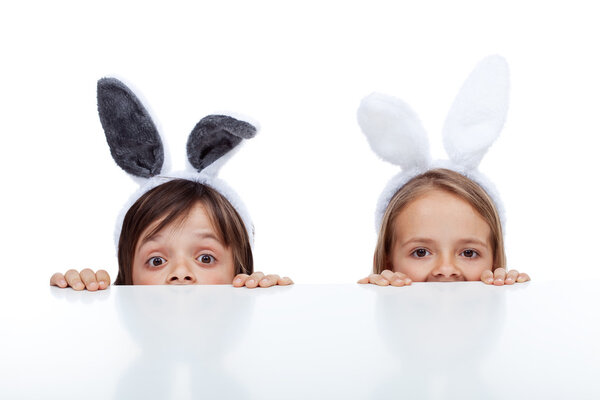 Дети с кроличьими ушами подглядывают из-под стола
