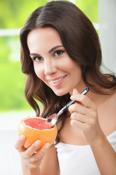 Mujer joven sonriente comiendo toronja en casa —  Fotos de Stock