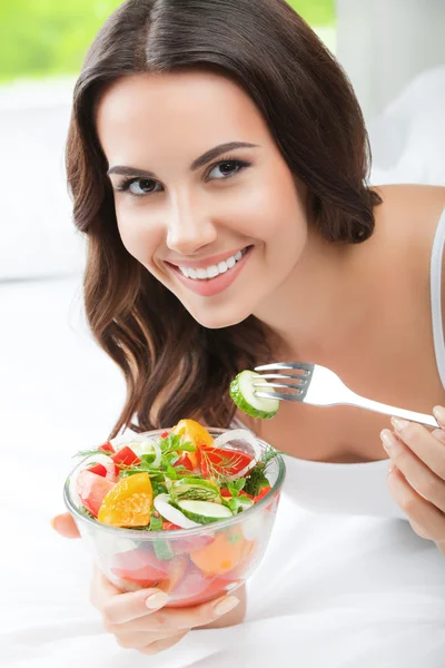 Sonriente joven mujer comiendo ensalada, en la cama —  Fotos de Stock