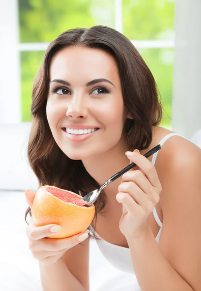 Lachende jonge vrouw eten grapefruit thuis — Stockfoto