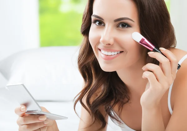 Mujer joven sonriente con cepillo de maquillaje, en el interior —  Fotos de Stock