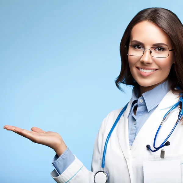 Young doctor showing something, on blue — Stock Photo, Image
